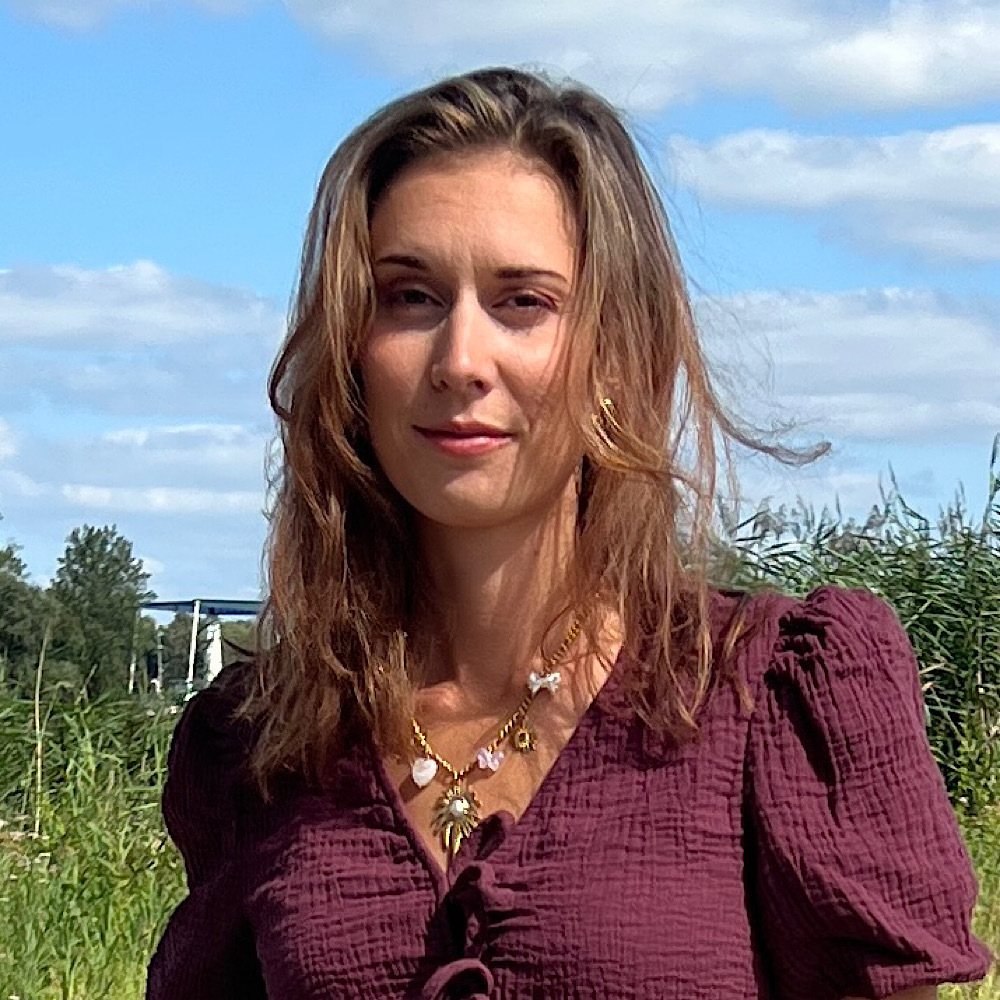 Close-up van vrouw met gouden oorbellen en kettingen met vlinder- en kruisbedels, in paarse blouse.