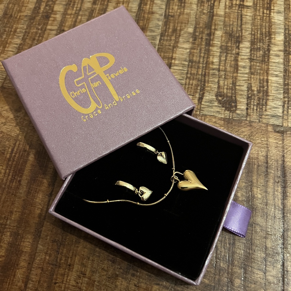 Paars sieradendoosje van Grace And Praise met gouden armband en ketting met hartje bedel op houten tafel, open deksel zichtbaar.