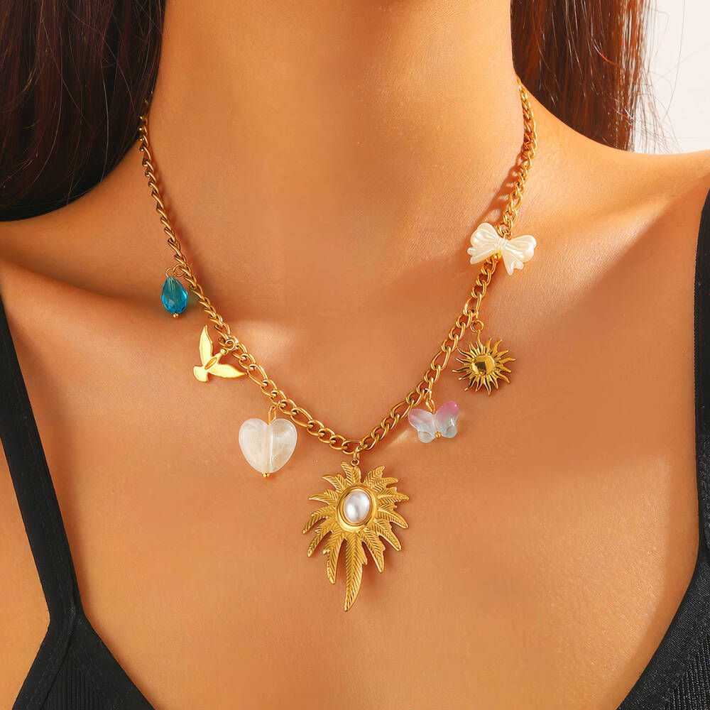 Gouden ketting met bedeltjes, waaronder zon, bloem, vlinder en parel, op blote hals. 18K verguld