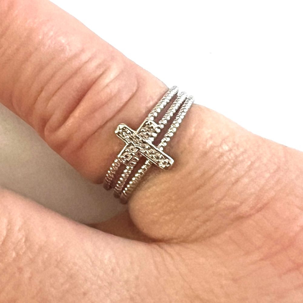 Zilveren kruisring met details op de vinger, close-up tegen witte achtergrond.