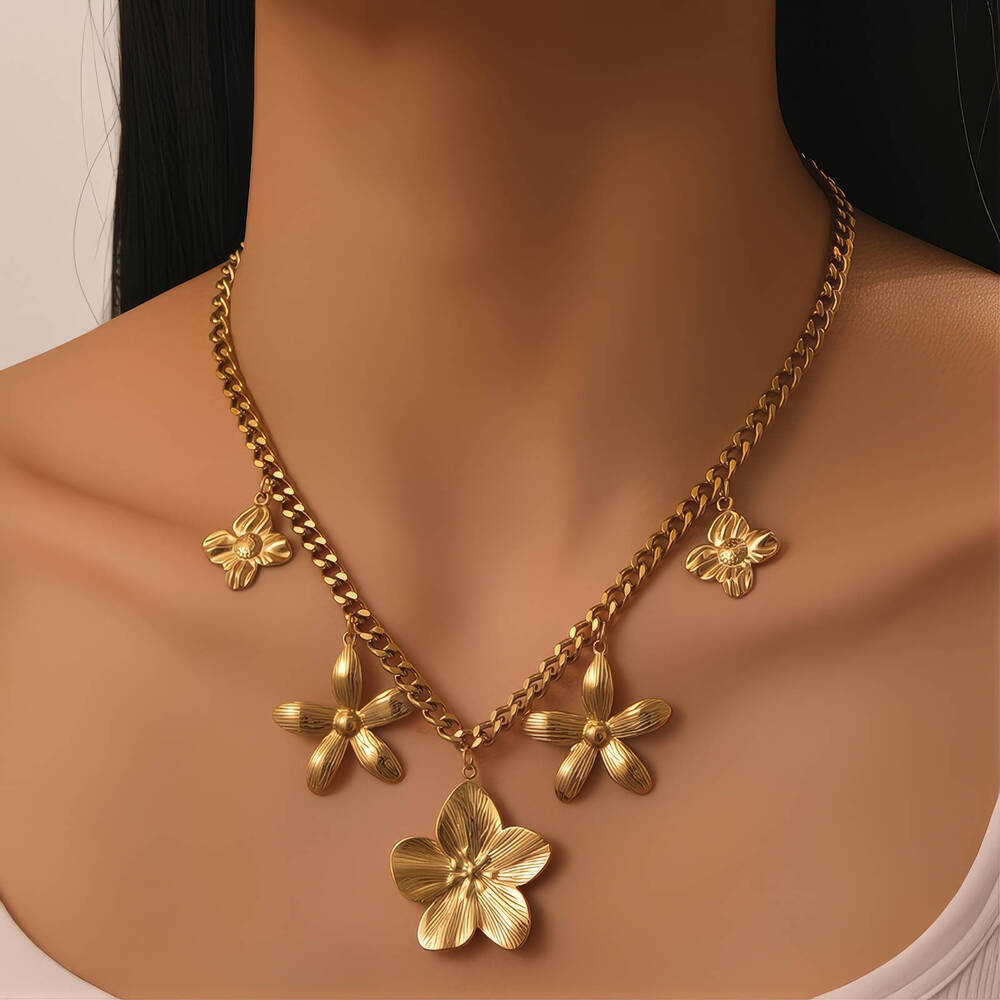 Gouden ketting met bloemvormige hangers, gedragen op blote schouders tegen donkere achtergrond.